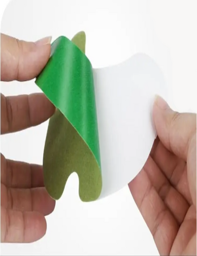 Green and white adhesive patch being peeled off a strip, held by hands on a white background.